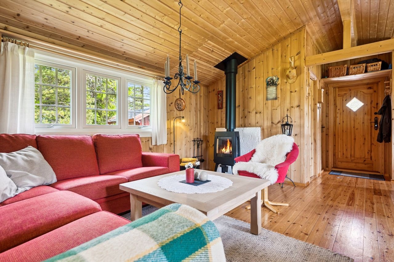 Stue med peisovn og gjennomgående trepanel gir en varm og innbydende atmosfære. Galleribilde