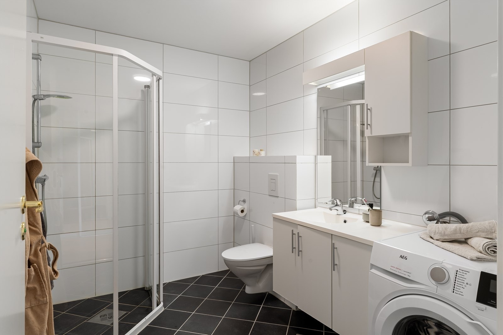 Baderommet er romslig, med tidløse fliser og varme i gulv for ekstra komfort. Opplegg for vaskemaskin og tørketrommel. Galleribilde