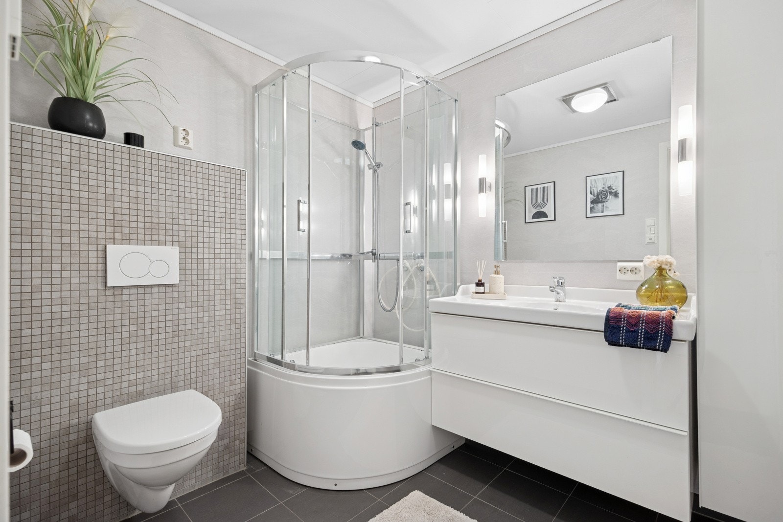 Det ca. 5 kvm store badet er innredet med våtromsplater på vegger og fliser på gulv. Badet er utstyrt med en pen baderomsinnredning med skuffeseksjoner, veggskap og nedfelt servant. Øvrig innredning består av dusjkabinett med badekar og vegghengt toalett. Galleribilde