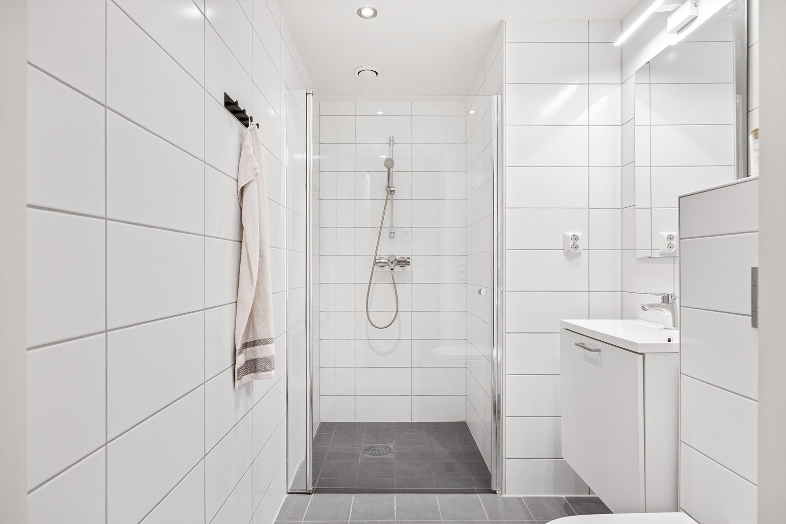 Boligens andre bad er perfekt som gjestebad og har dusjnisje med glassdør, vegghengt toalett, og vegghengt servant med underskap og speil. Galleribilde