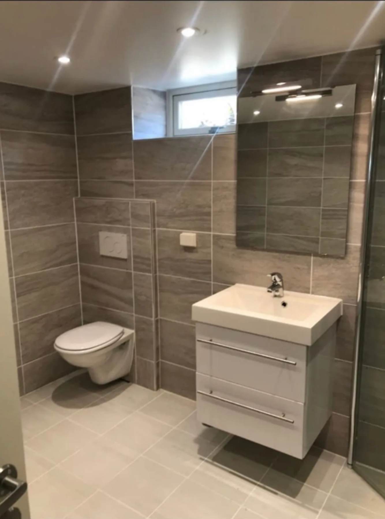 Lekkert bad fra 2022 med fliser i dus varme toner, gulvvarme og moderne innredning. Badet er innredet med vegghengt toalett, dusjhjørne og god oppbevaring i servantskapet. Galleribilde