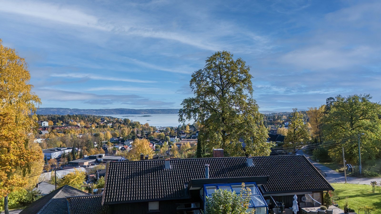 Åpen og luftig utsikt mot nærliggende hus og natur. Bildet er tatt ca. 5 meter over bakkenivå fra nabotomt. Galleribilde