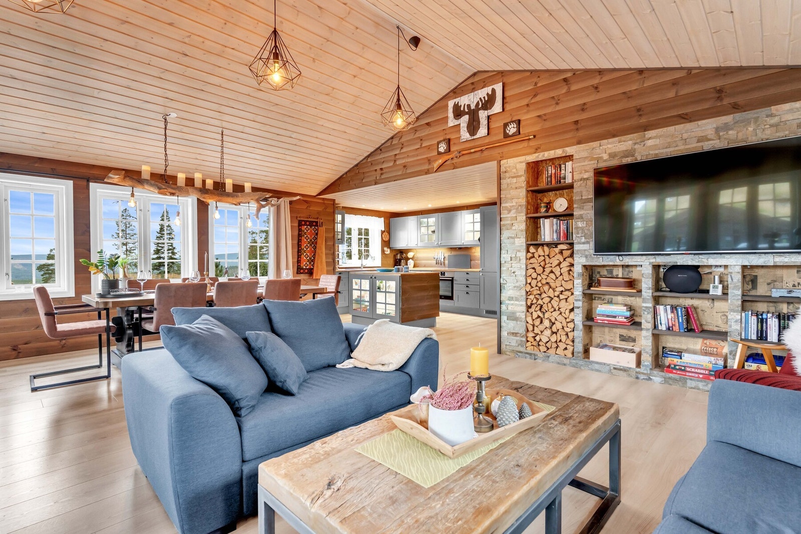 På ene veggen finner du en stilfull flislagt kontrastvegg med innebygd vedstativ og hyller, inkludert plass til TV - praktisk, funksjonelt og samtidig dekorativt. Galleribilde