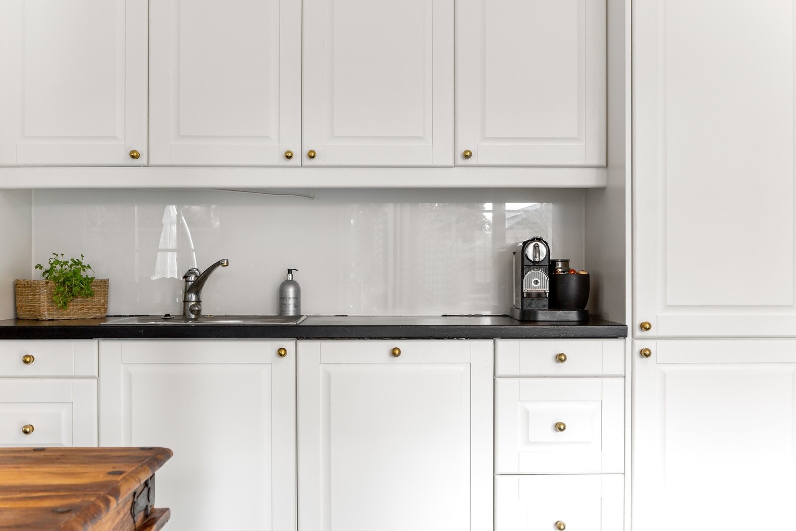 Innredningen har hvite, profilerte fronter med messingknotter, kombinert med sortmalt benkeplate i heltre og lyse glassplater som backsplash. Galleribilde