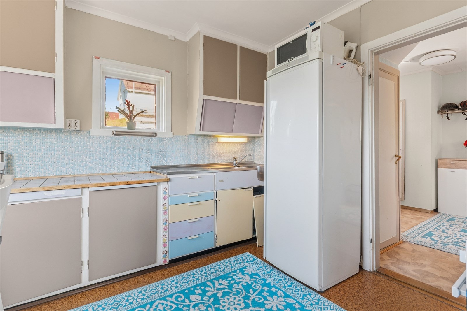 Kjøkkeninnredning med malte, slette fronter, dobbel stålvask med benkebeslag og fliser på vegg over benk. Galleribilde