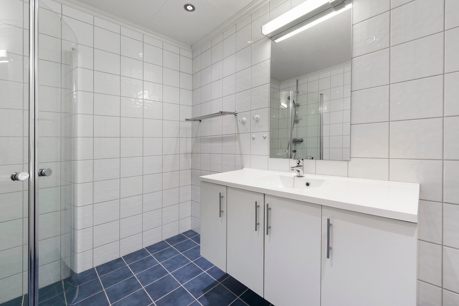 Bad i underetasje med flislagt gulv med varme i. Baderomsinnredning med heldekkende servant og dusjhjørne Galleribilde