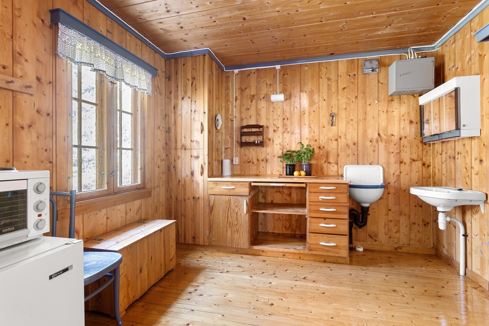 Eldre, enkelt hyttekjøkken med innredning i glatte furufronter og benkeplate i heltre. Galleribilde