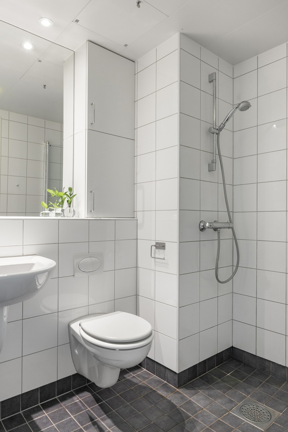Badet er innredet med vegghengt toalett, servant med speil og dusjhjørne. Galleribilde