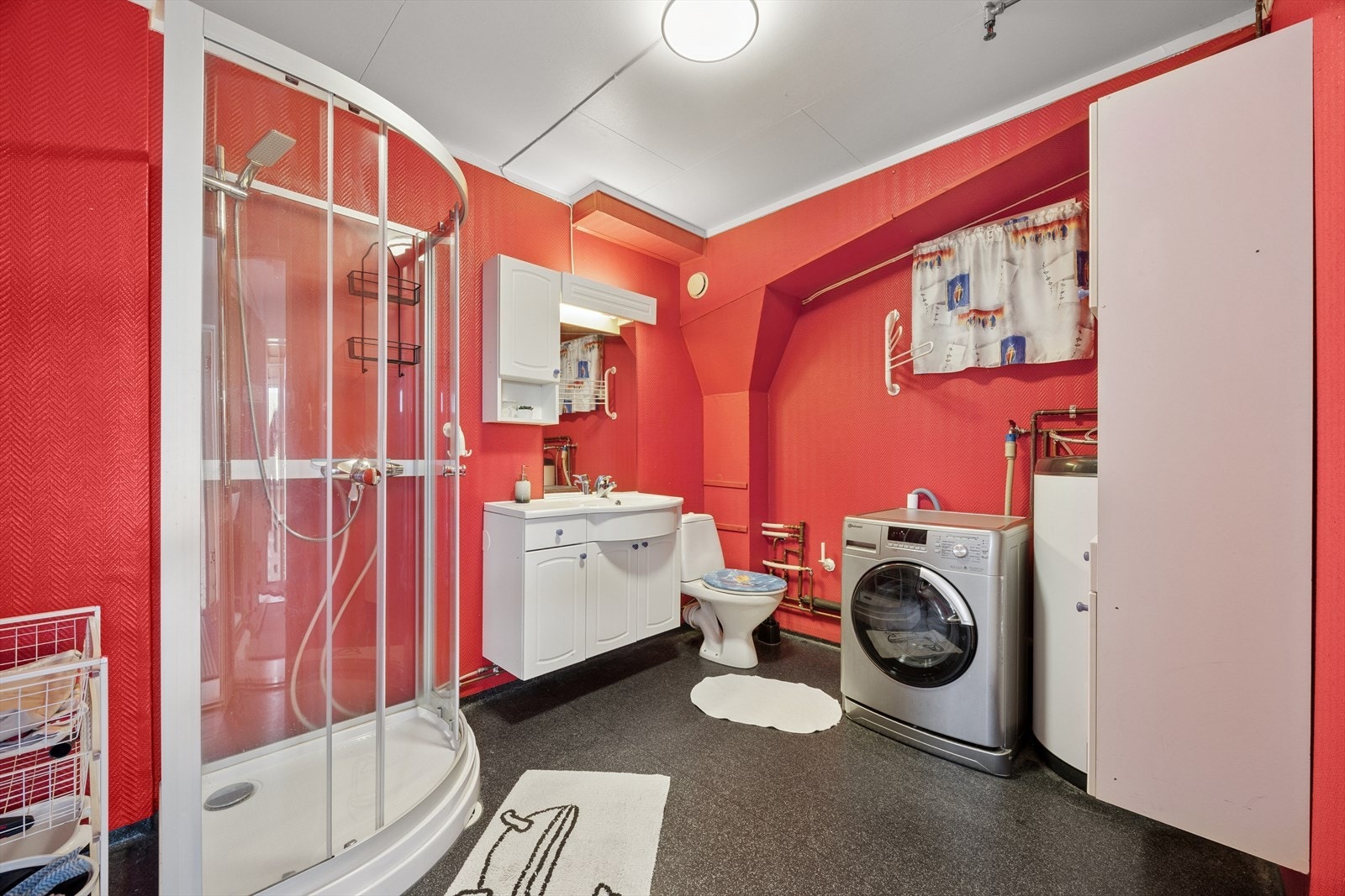 Et romslig og funksjonelt baderom med dusjkabinett, toalett, servant med innredning, speil med belysning og opplegg for vaskemaskin. Galleribilde