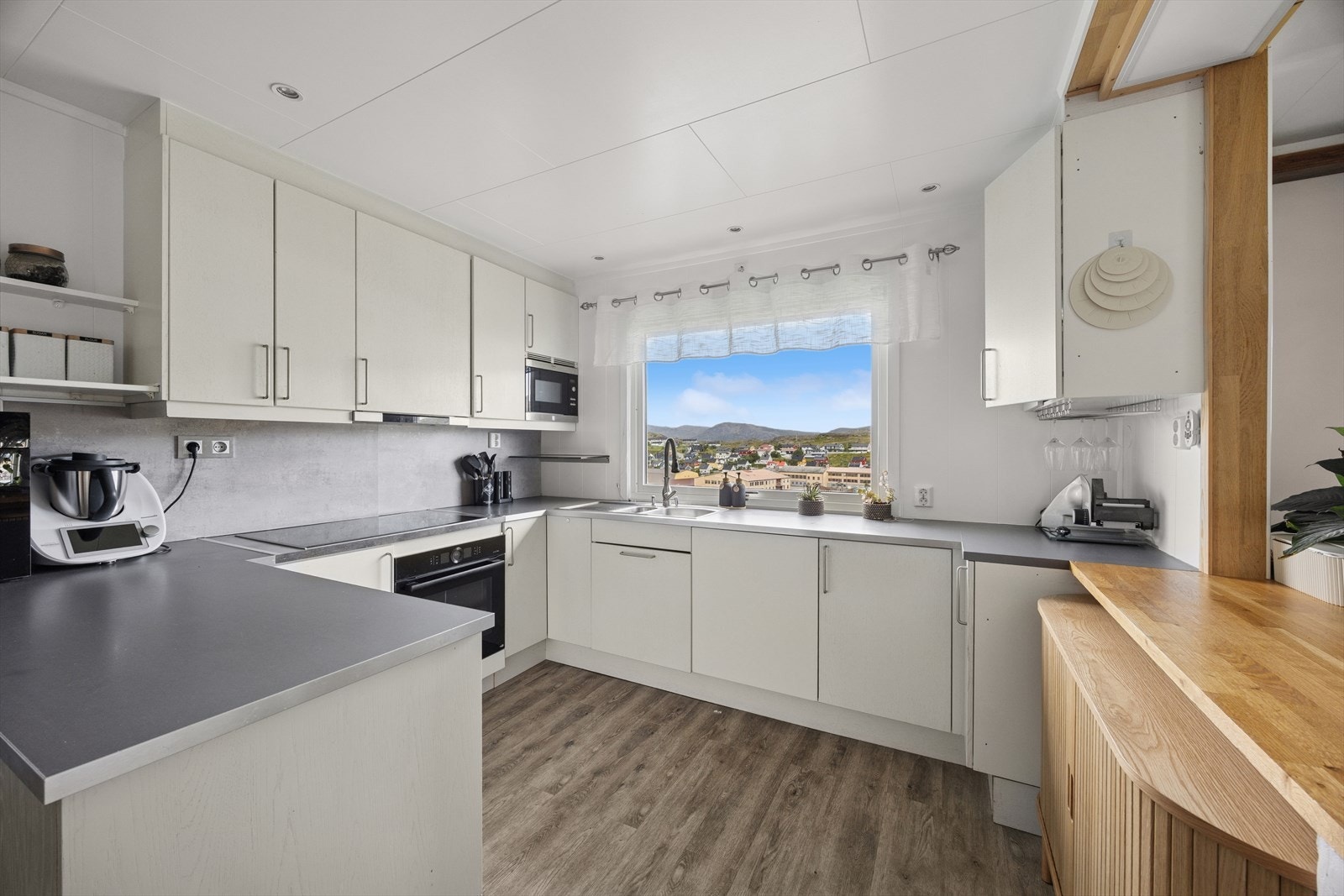 Kjøkkenet har takhøye skap og gode arbeidsforhold. Her finner du alt du trenger for en effektiv hverdag. Et åpent felt i vegg mot stue sørger for gode lysforhold. Galleribilde