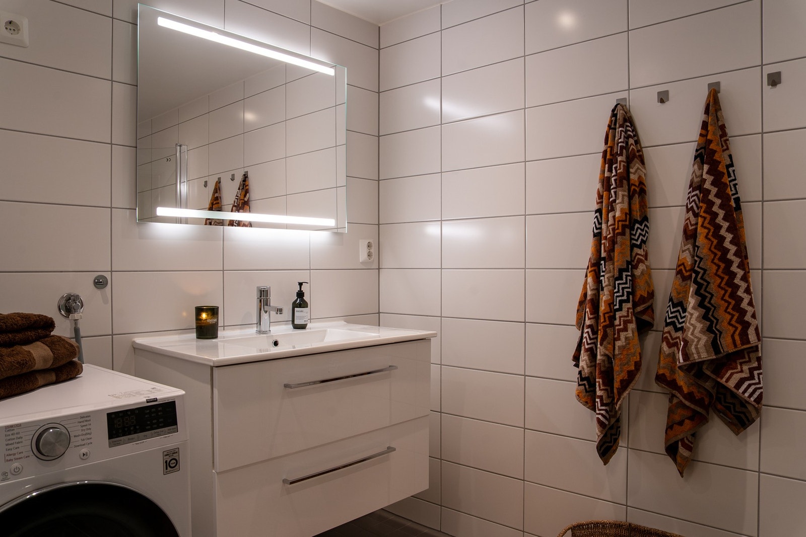 Baderomsinnredningen består av servant på lys skuffeinnredning samt speil, dobbel stikk og lys på overside. Videre er det vegghengt toalett og dusjhjørne med svingbare dører som frigjør plass på gulvet. Galleribilde