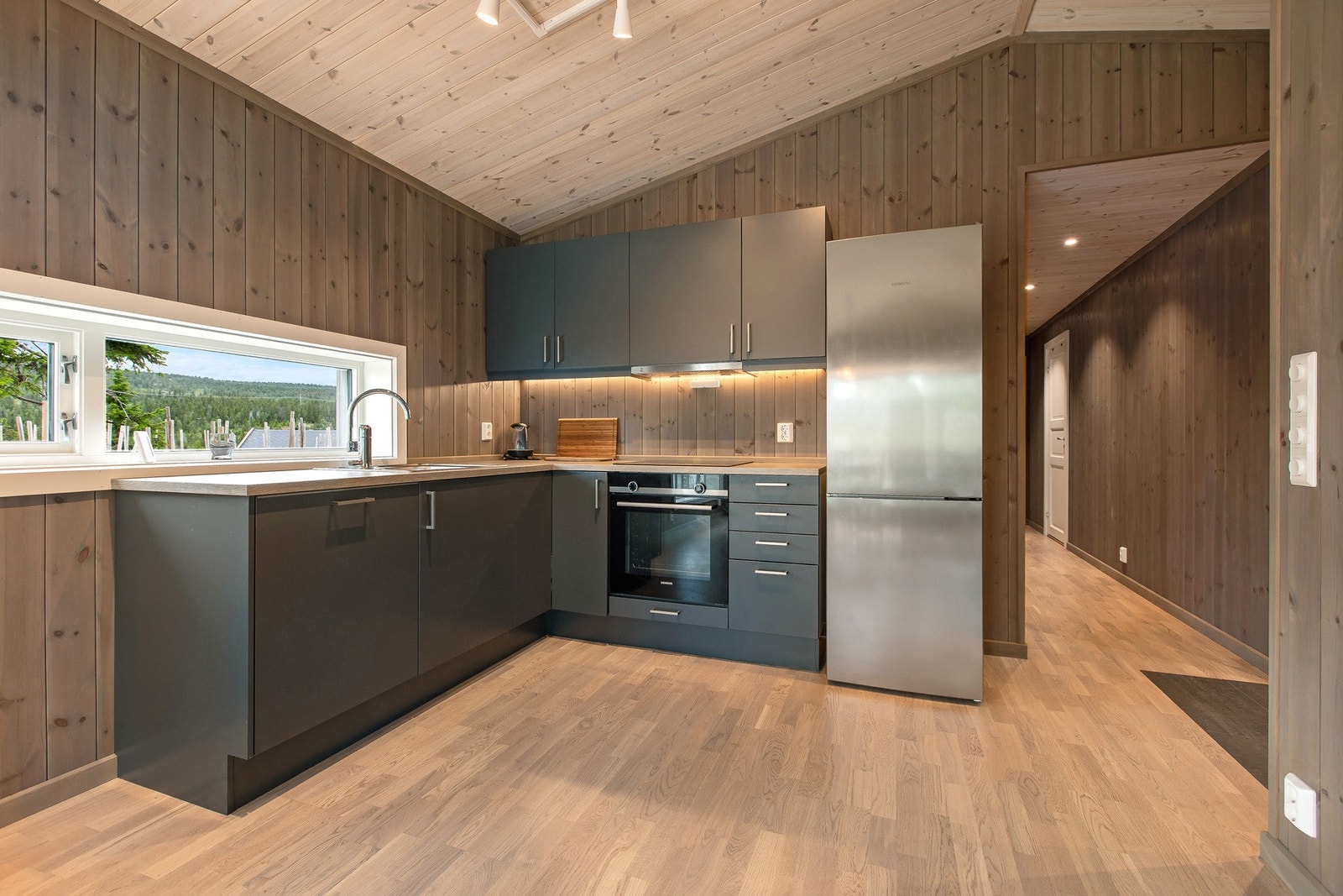 Moderne kjøkkeninnredning i mørk grå matt finish, integrerte hvitevarer, vindu over benken og god skapplass. Galleribilde