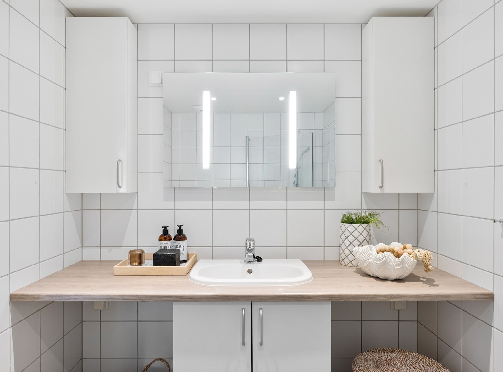 Praktisk innredning med heldekkende servant, speil med integrert belysning og romslig dusjhjørne med glassdører. Galleribilde