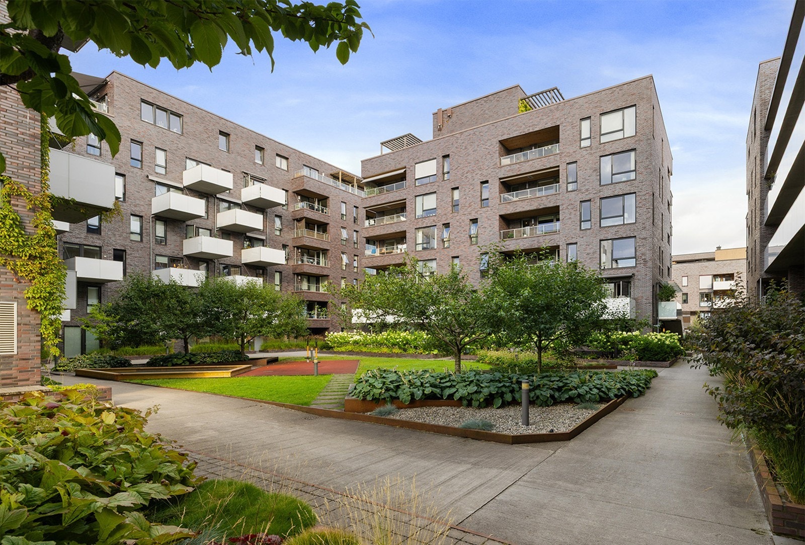 Velstelt og frodig felles gårdsrom med plenarealer, prydbusker, trær og sitteplasser - et rolig og grønt avbrekk midt i byen. Sameiet består av moderne bygg med stilren teglfasade. Galleribilde