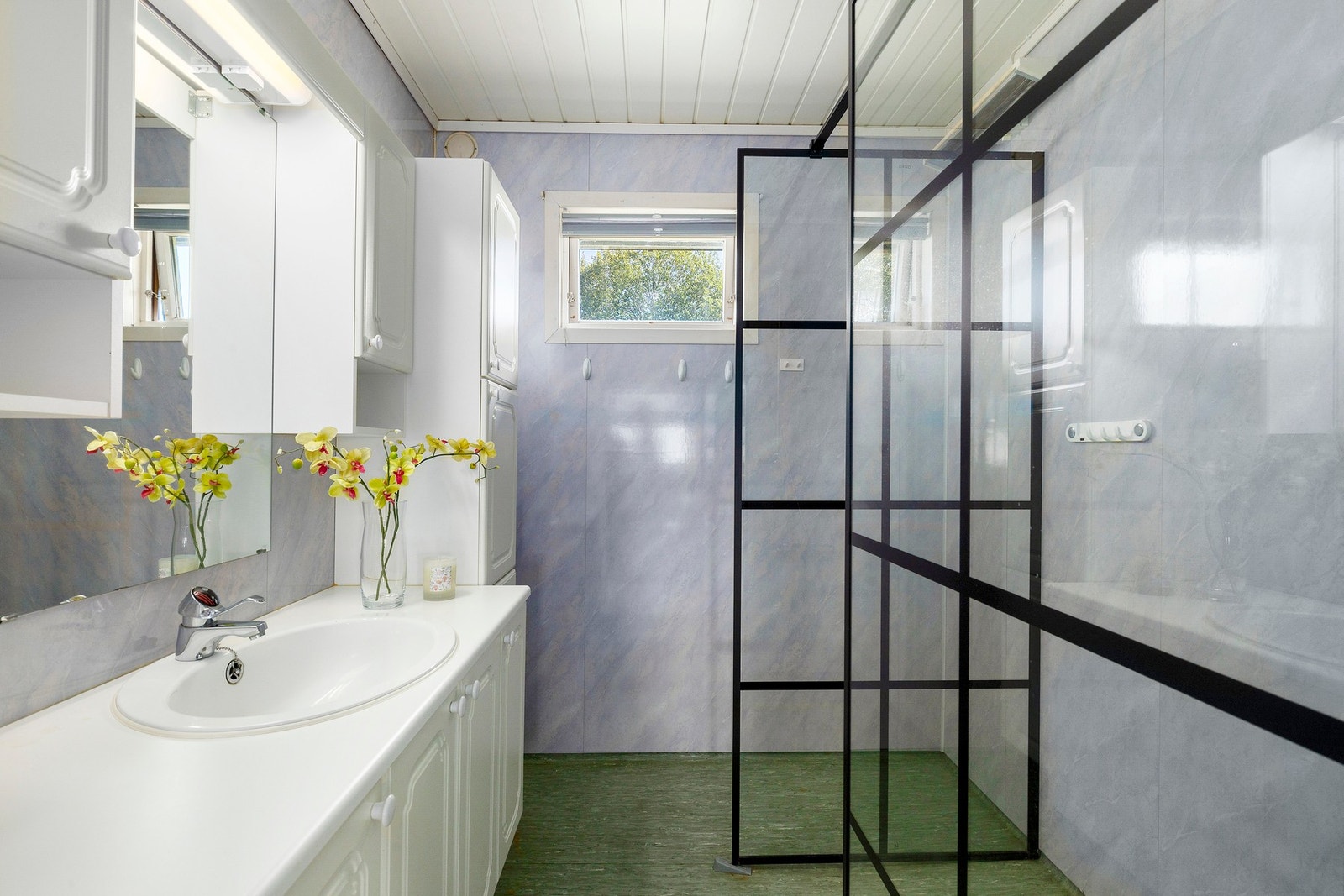 Baderom i hovedetasje med servantskap og dusjhjørne. Det er belegg på gulv og våtromsplater på vegger. Galleribilde