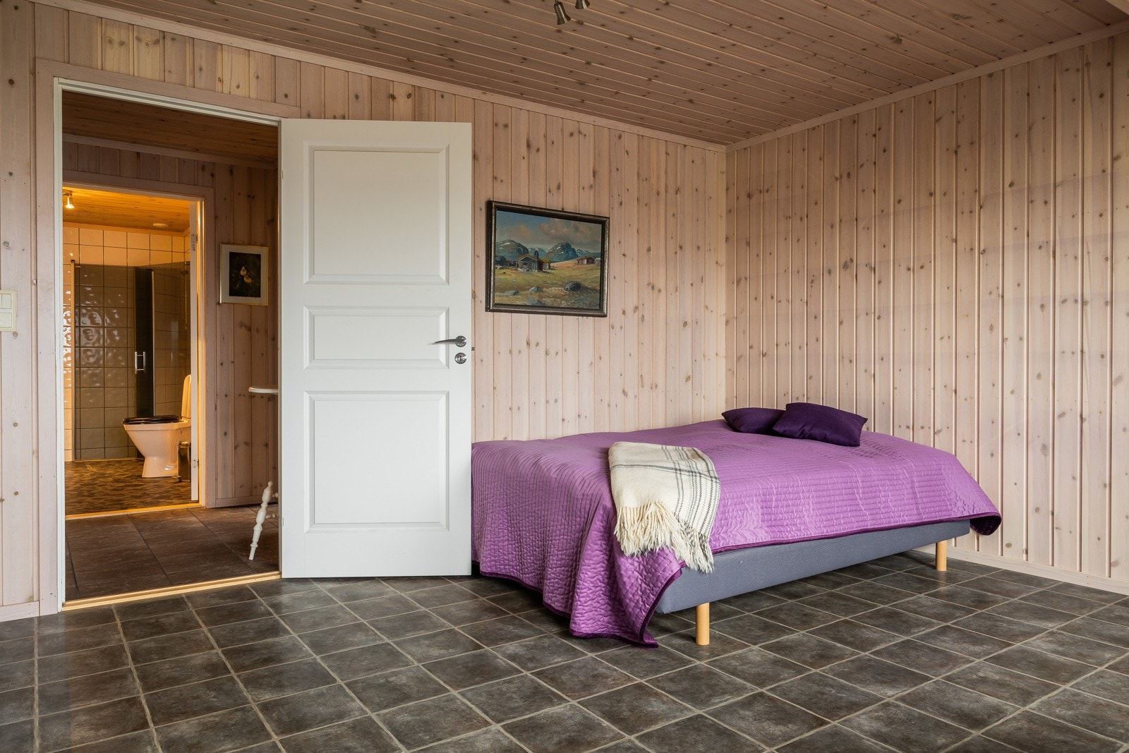 Ett av soverommene i underetasjen skiller seg ut med varme trepaneler på veggene, som tilfører et sjarmerende og koselig preg. Galleribilde