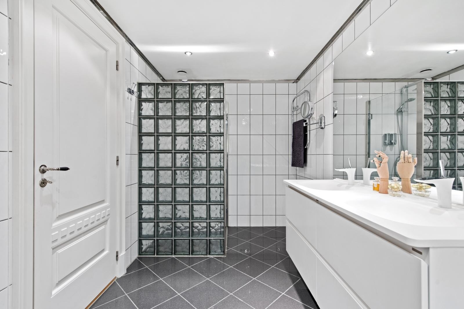 Badet er utstyrt med dusjhjørne m/ glassvegg, flislagt badekar, vegghengt toalett, innredning dekket med benkeplate med 2 stk. servanter og speil. Galleribilde