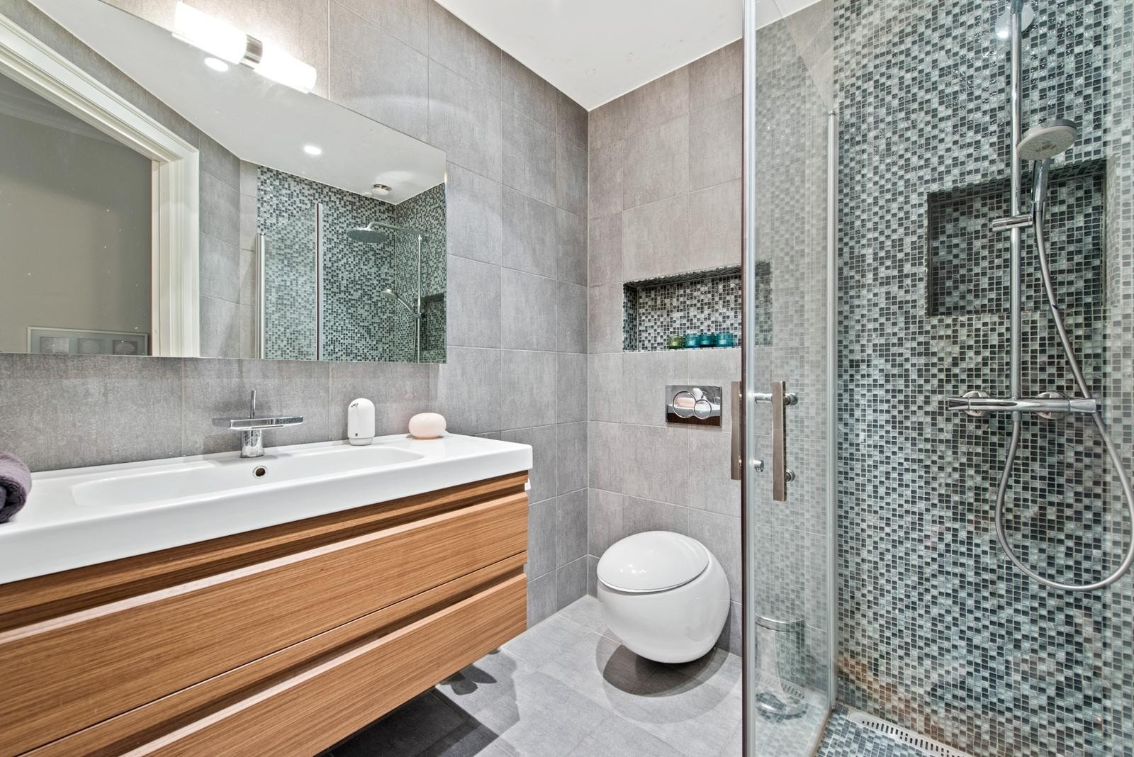 Bad med adkomst fra soverommet er helfliset med downlights i himling og varmekabler i gulvet. Badet er fra 2014 og utstyrt med innredning med heldekket servant med speil og lys, vegghengt toalett og dusjhjørne med innfellbare dører. Galleribilde