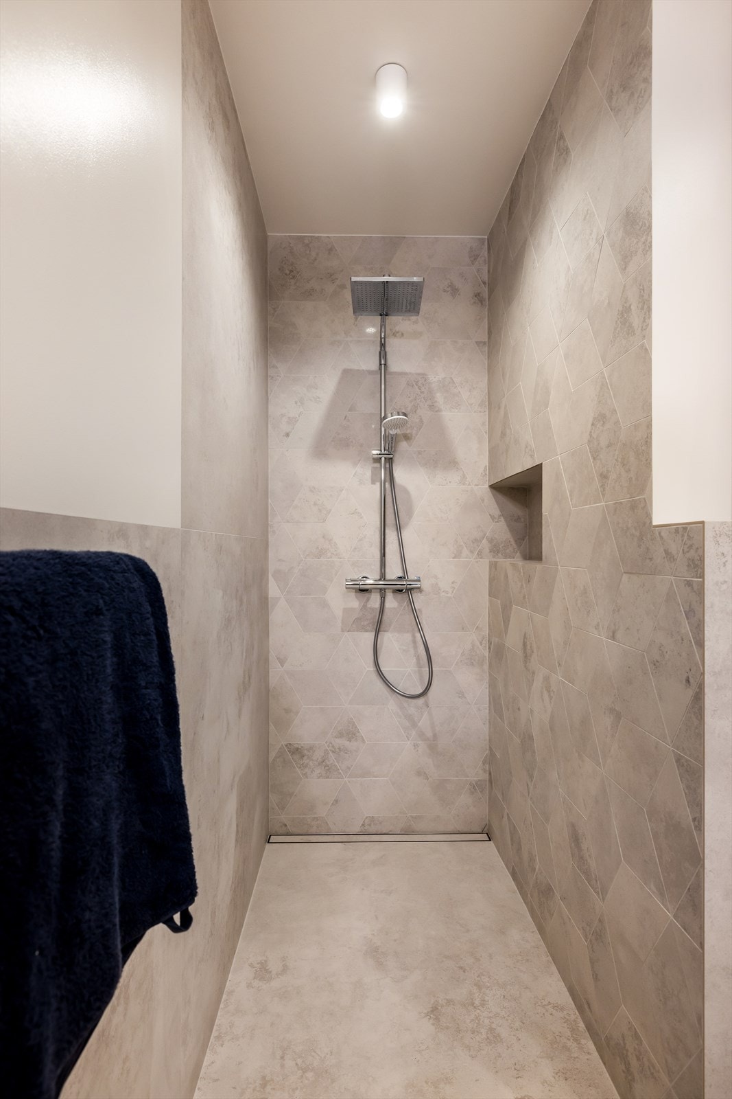 Egen dusjnisje med mosaikkfliser, takdusj og veggnisje for oppbevaring av velværeprodukter. Galleribilde