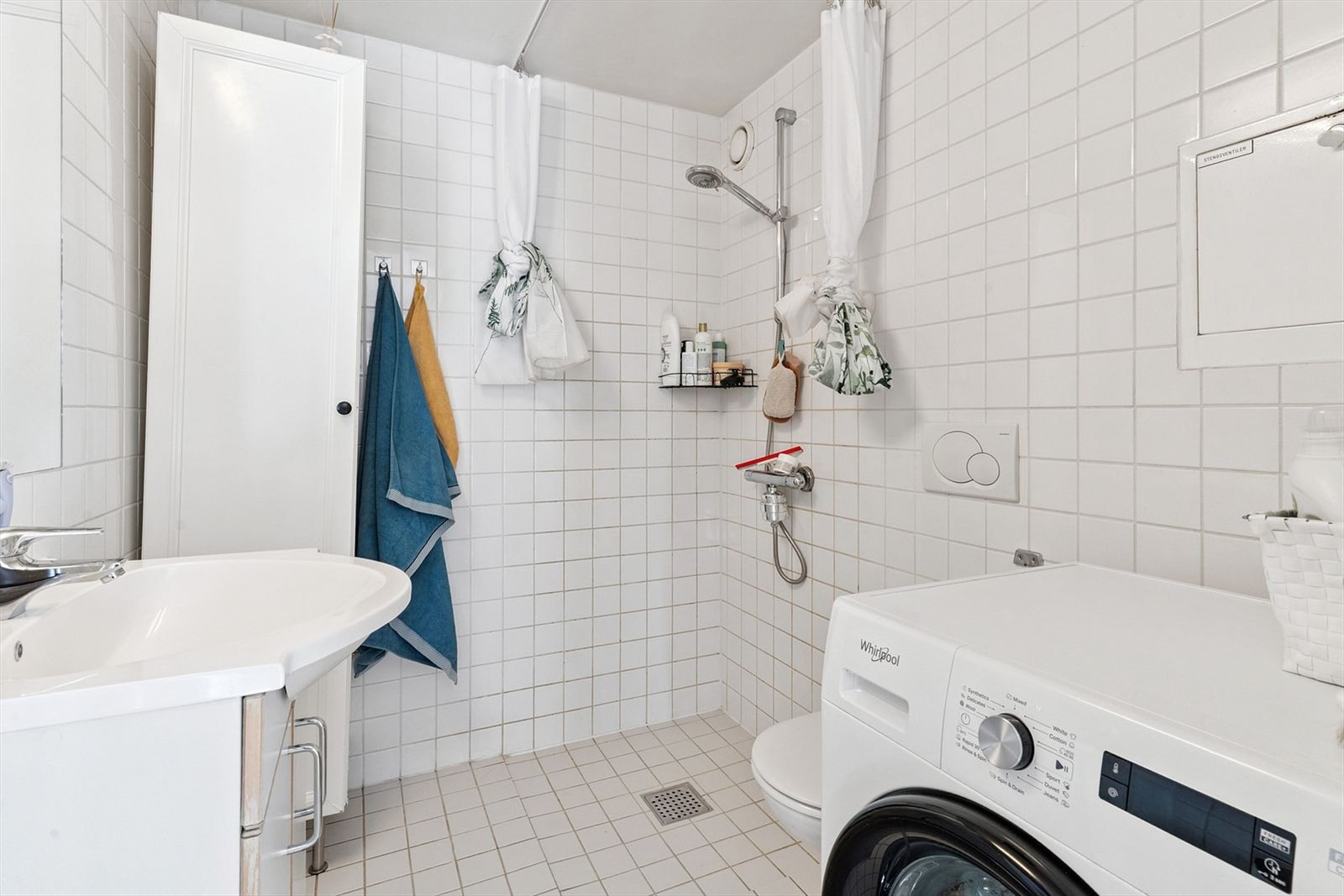 Pent flislagt baderom med dusj, wc, servant, speil og oppvaskmaskin. Galleribilde