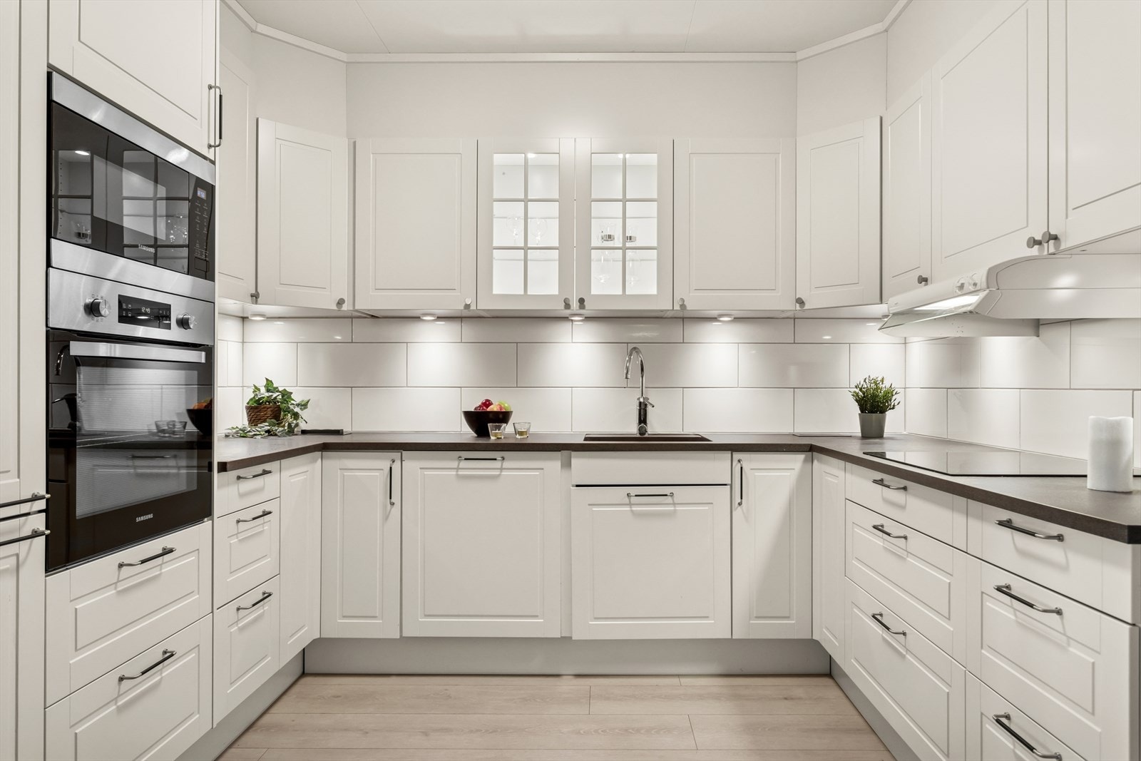 Velutstyrt og fint kjøkken med profilerte fronter og laminat benkeplate med underlimt oppvaskkum og nedfelt platetopp. Flis på vegg over benkeplate. Kjøkkenventilator med avtrekk ut. Galleribilde