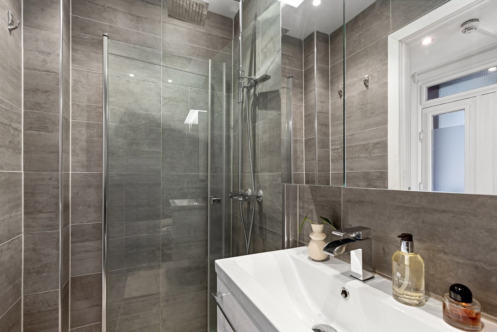 Innredet med toalett, hjørnedusj med regnfalssarmatur og innsvingbare glassdører, speilskap og servant med skuffer. Galleribilde