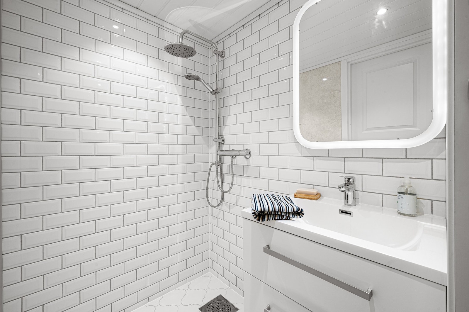 Badet er innredet med dusjhjørne og speil med integrert lys over servant. Galleribilde