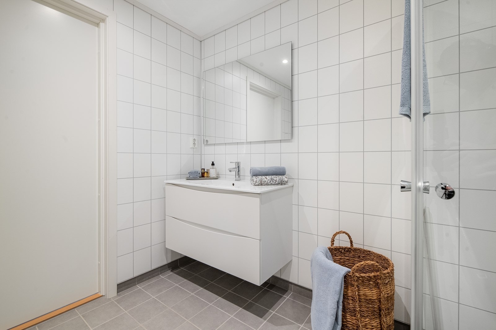 Leiligheten har et romslig bad med flislagt gulv og baderomsplater på veggoverflatene, gulvvarme i gulv. Her er det en stilren innredning med dype skuffer og heldekkende servant, samt speil på vegg. Galleribilde