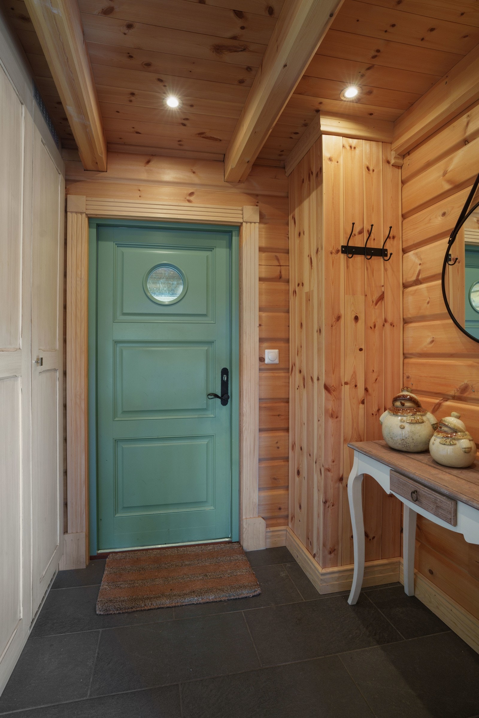 Entreen har laftede tømmervegger, downlights i himlingen og koksgrå fliser på gulvet. Yttertøy, sko og utstyr ryddes enkelt bort i en romslig garderobeløsning med lyse, profilerte fronter. Galleribilde