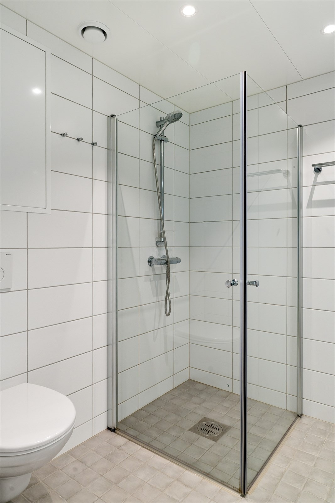 Videre er badet innredet med servantskap med overskap og speil med lys, vegghengt toalett og dusjhjørne. Galleribilde