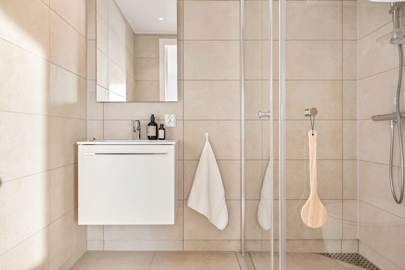 Badet er helfliset med spotter i tak, elektrisk varme i gulvene og innredet med dusj i hjørnet, vegghengt toalett og servant med speil og belysning. Galleribilde