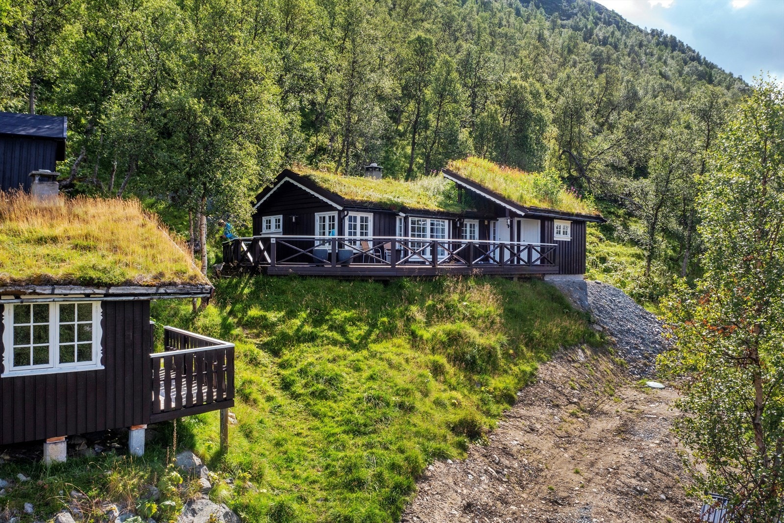 Hovedhytta på eiendommen inneholder romslig vindfang, stue med åpen kjøkkenløsning, bad, to soverom, hems og utvendig bod Galleribilde