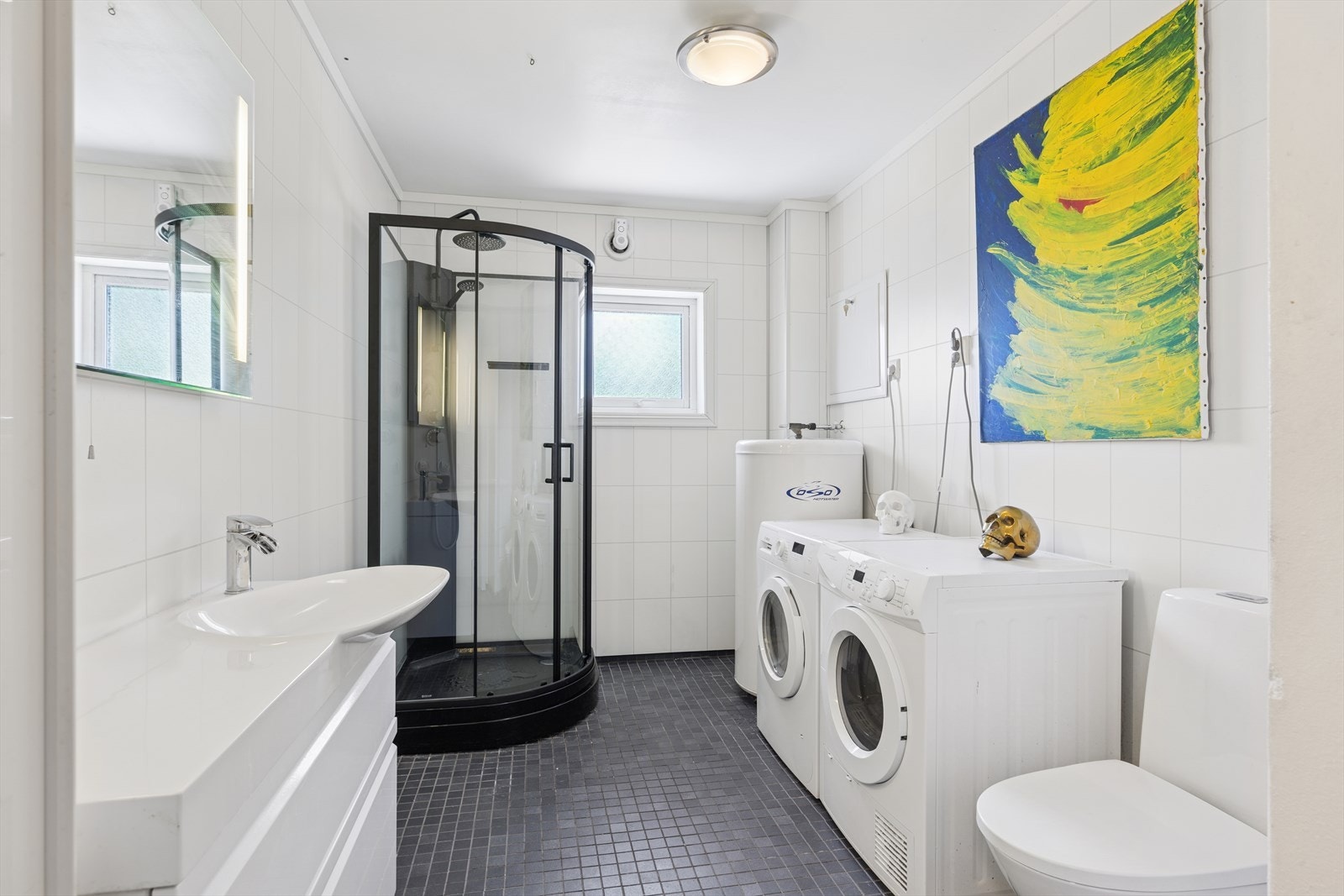 Badet er flislagt på gulv, baderomsplater på vegger og har nytt dusjkabinett (2025), wc, vask og opplegg for vaskemaskin. Galleribilde