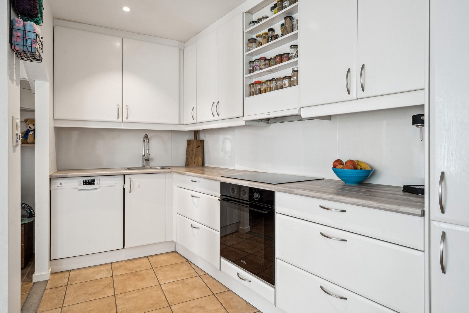 Kjøkken med slette hvite fronter og mye oppbevaringsplass i høye overskap og dype skuffer. Galleribilde