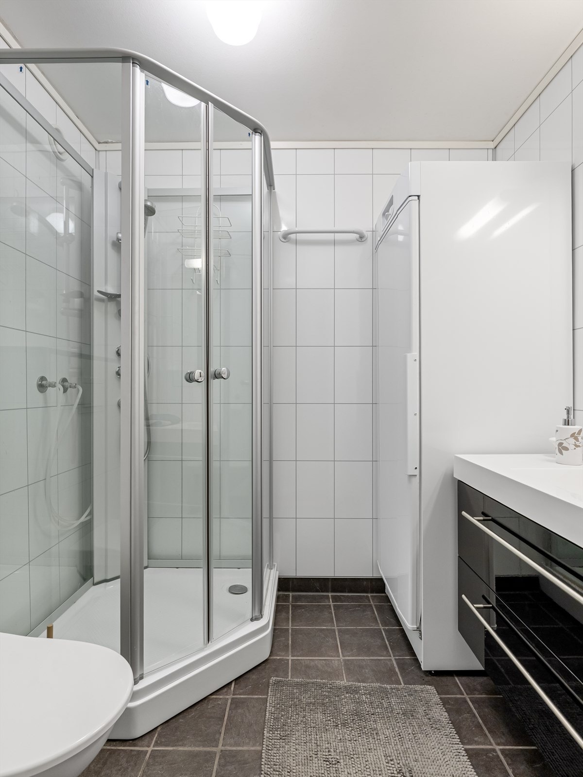 Bad med fliser, praktisk tørkeskap, vask i seksjon, speil med lys, dusjkabinett og vegghengt wc. Galleribilde