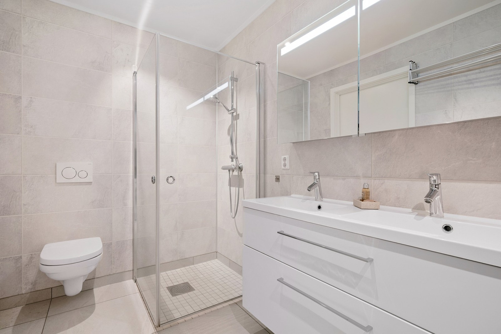 Boligen har ett bad i hver etasje. I underetasjen er bad og vaskerom i ett - med dusjhjørne, dobbel servant og vegghengt toalett - ideelt for familiens morgenrutiner Galleribilde