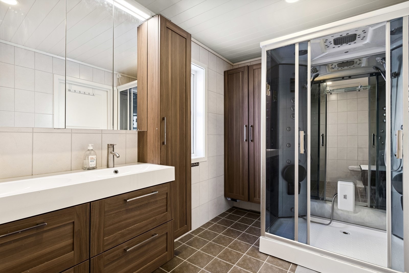 Baderommet er ca 7,7 m² og har flis på gulv og vegg, trepanel i himling. Oppgradert i 2014. Badet inneholder dusjkabinett, gulvmontert toalett samt innredning med servant Galleribilde