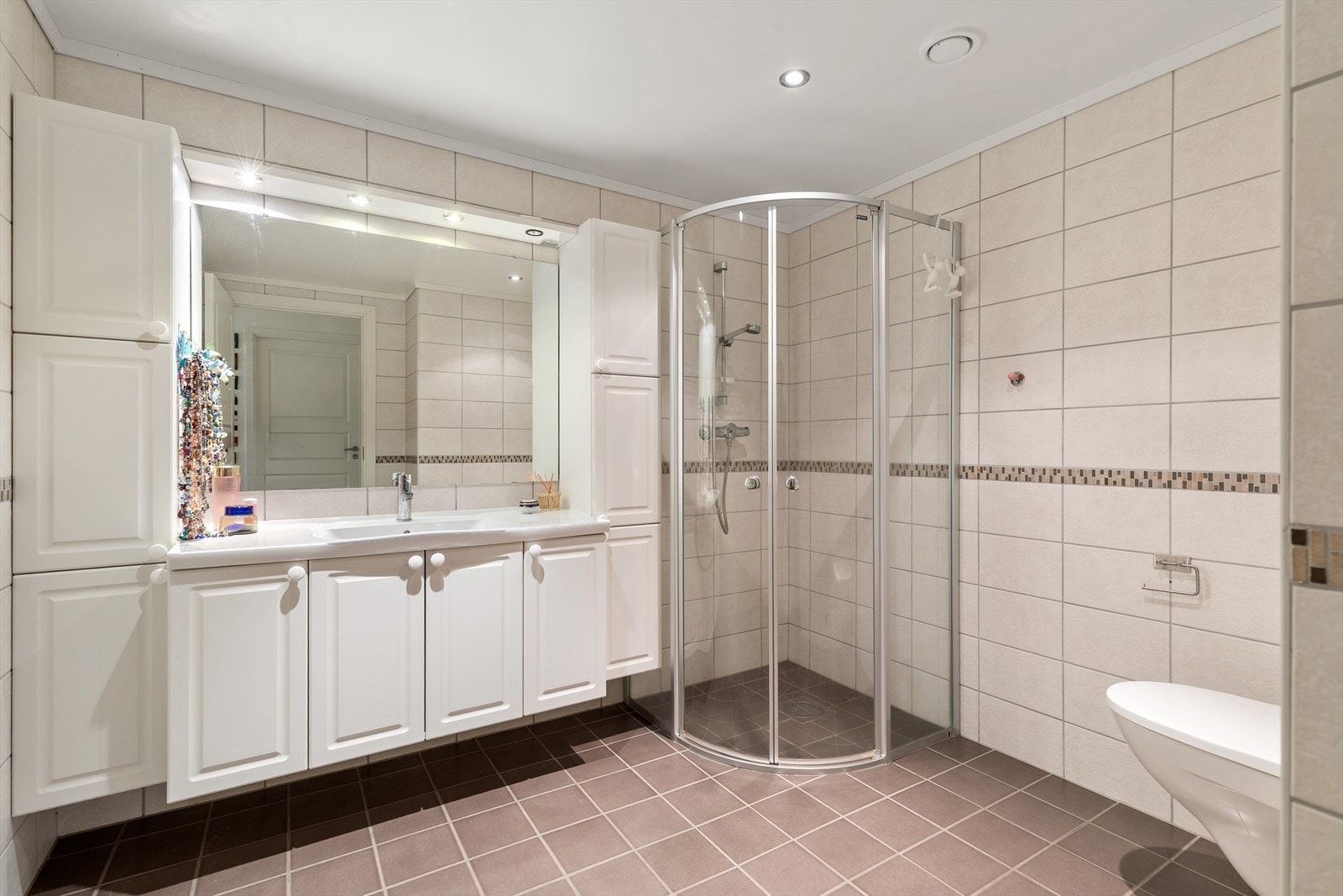 Badet er helfliset med fliser på både gulv og vegger. Det er vegghengt toalett med innebygd sisterne og dusjsone med innfelte dusjdører i herdet glass. Rommet har varmekabler i gulv. Galleribilde