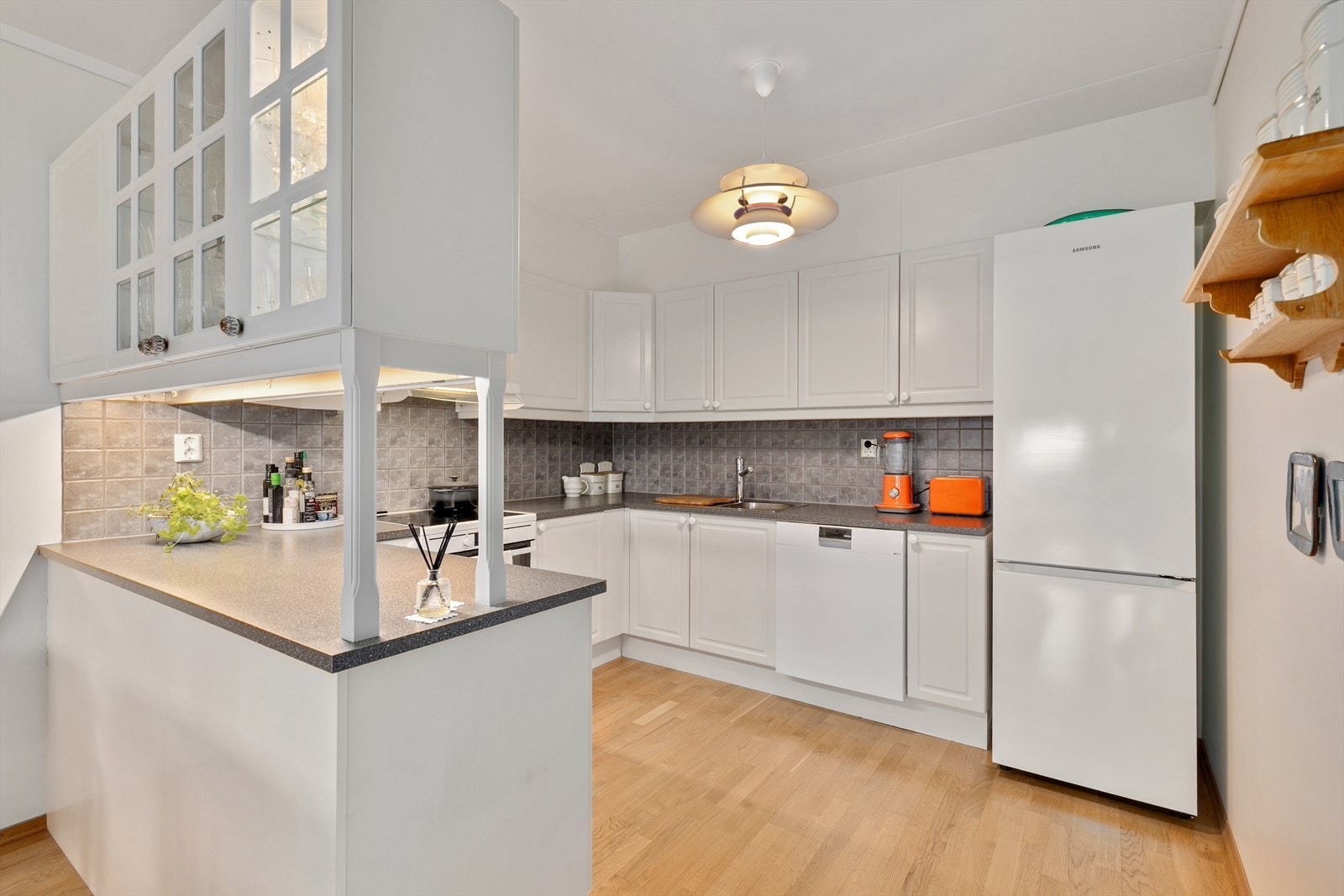 Kjøkkenet har innredning fra byggeår med hvite, glatte fronter. Løsningen består av både over- og underskap som gir gode oppbevaringsmuligheter, og det er montert belysning under overskapene. Galleribilde