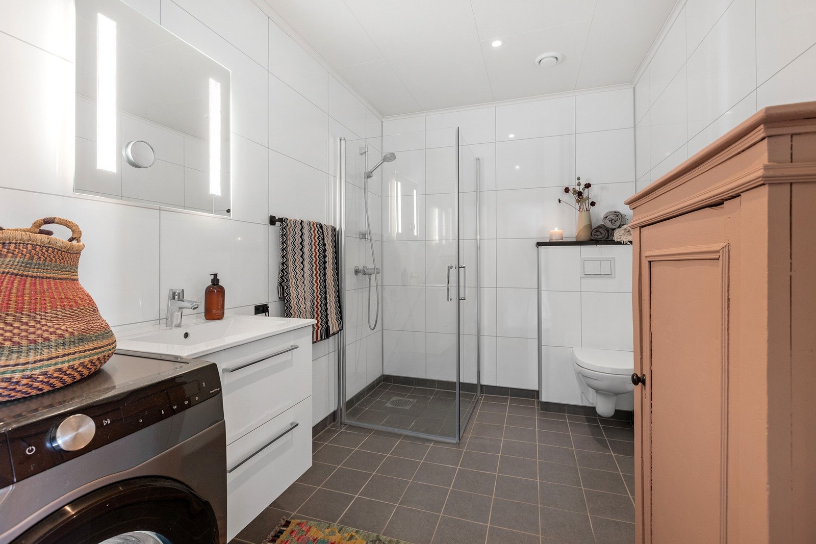 Moderne innredning og speil med belysning. Dusjvegger og vegghengt toalett. Plass til vaskemaskin. Galleribilde