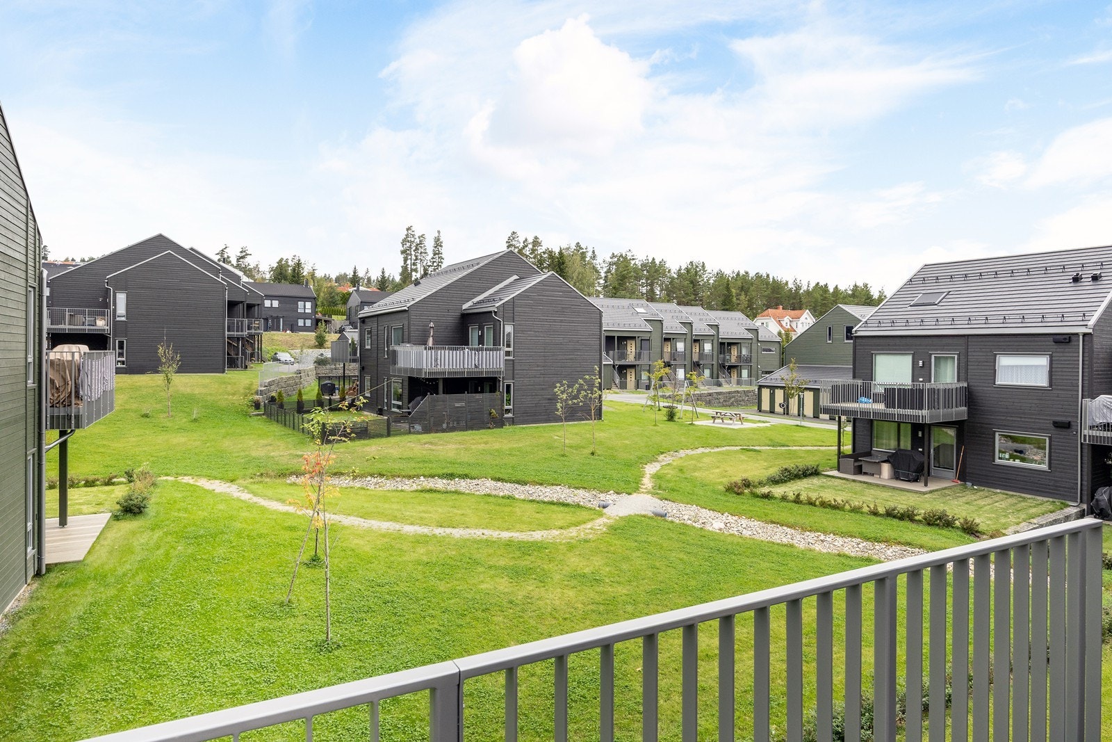 Fra balkongen er det trivelig utsyn ut mot et pent opprabeidet fellesareal med plen, beplantning og koselig gruslagt internvei. Galleribilde