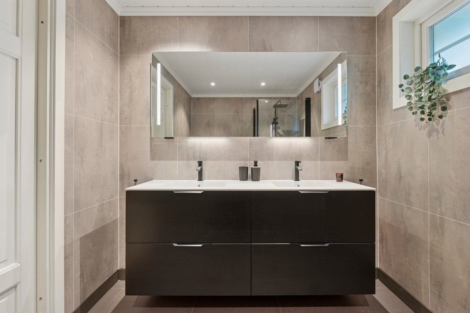 Badet er utstyrt med et dusjhjørne med innfellbare glassdører, og en elegant servantinnredning med doble servanter og rikelig lagringsplass i skuffer. Galleribilde