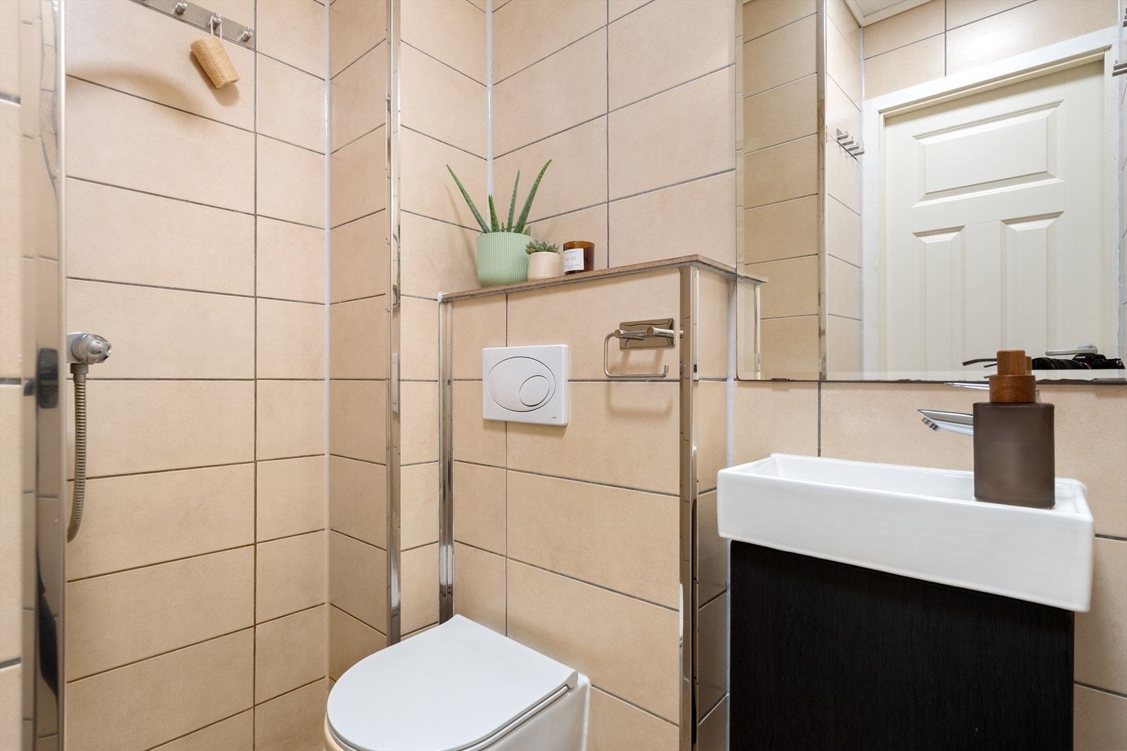 Praktisk helfliset bad innredet med vegghengt toalett, servant i møbel, overhengt speil og dusjhjørne. Galleribilde