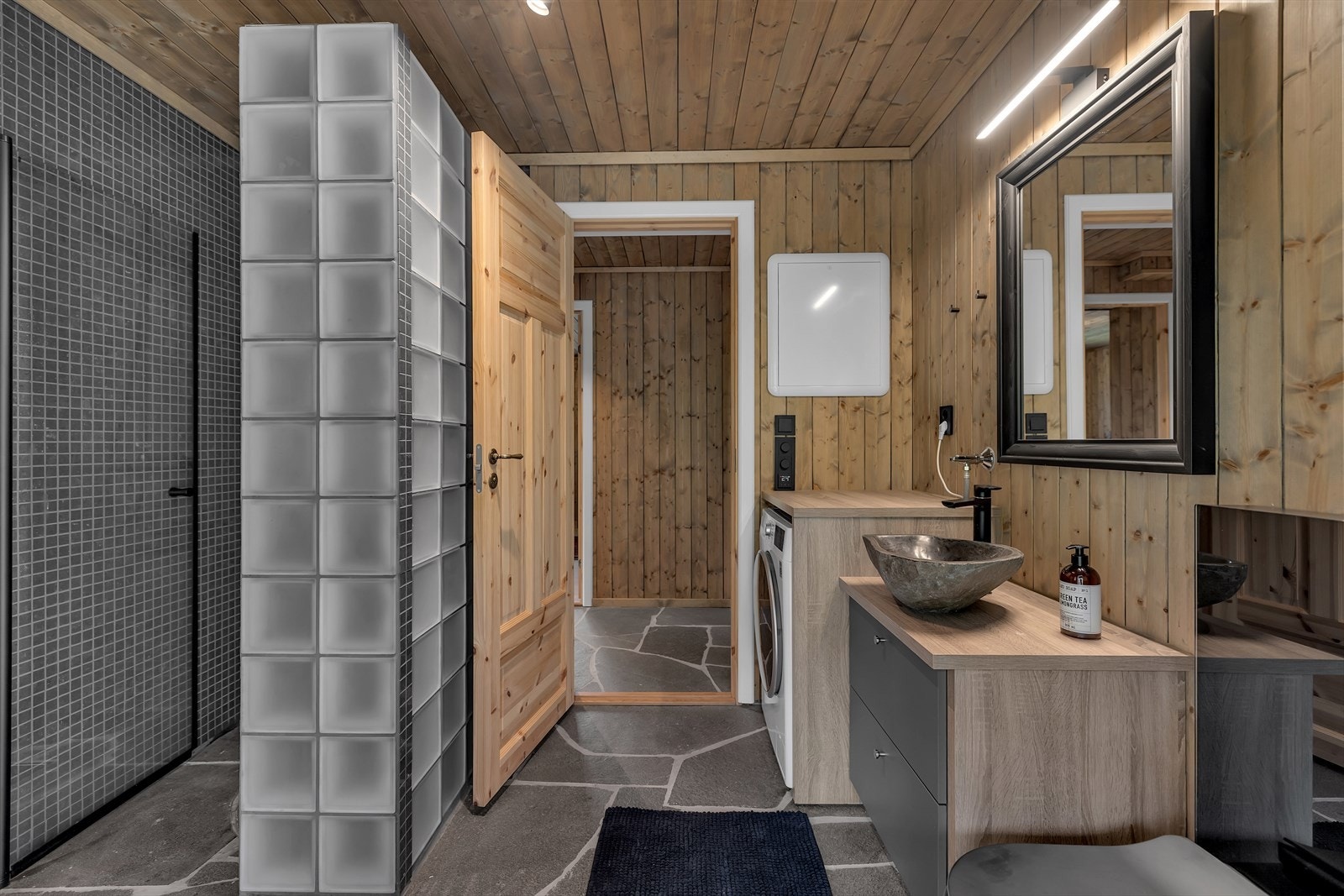 Flott badrom med eikedetaljer og sort garnityr på VVS og El. Legg merke til helhetlig preg i skifterfliser på baderom og gang/mellomgang. Galleribilde