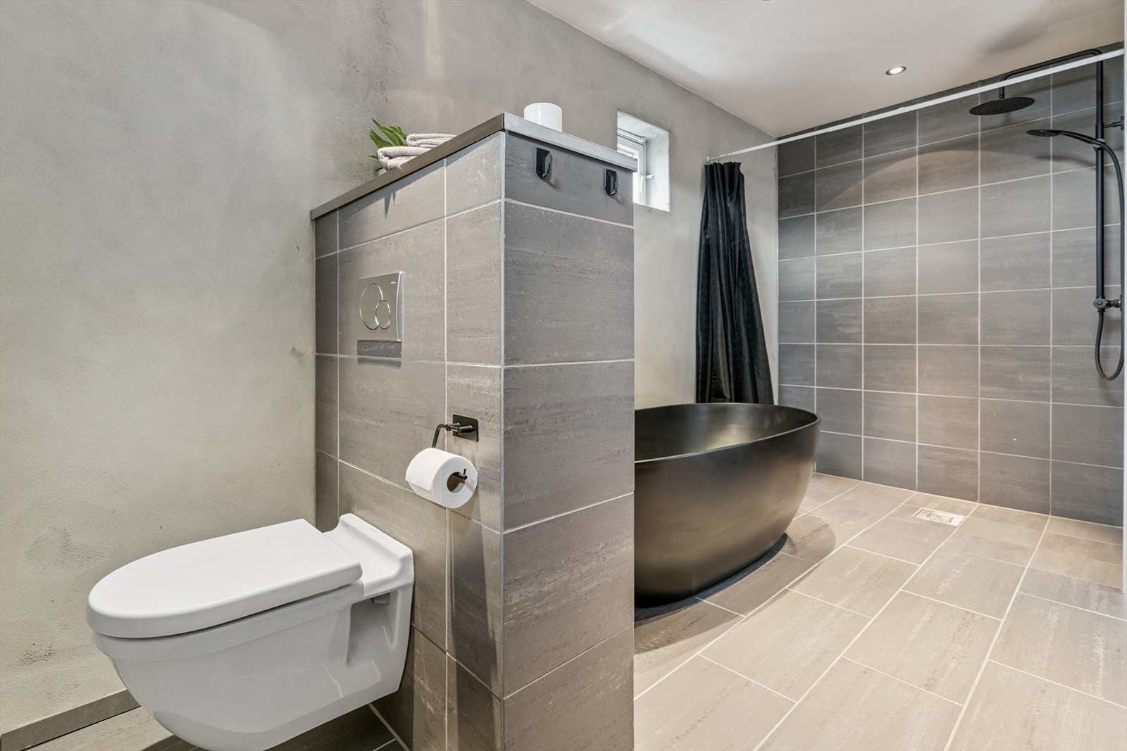 Baderom med badekar, dusj, vegghengt toalett og servant med innredning og speil Galleribilde