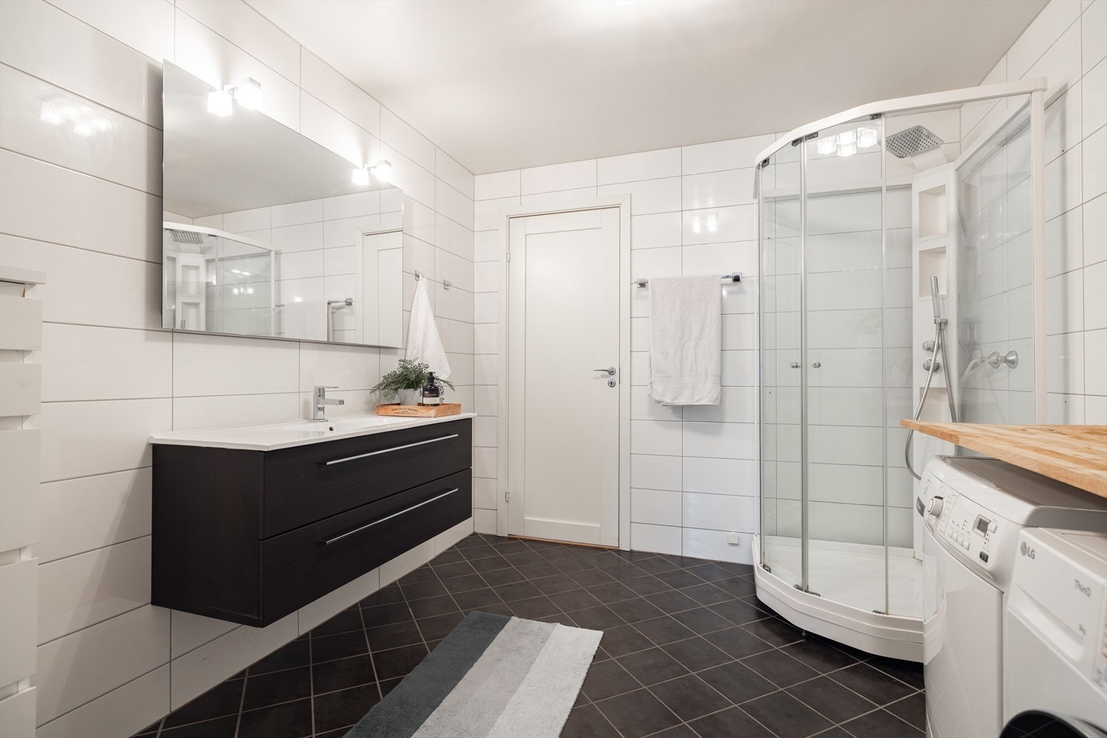 Badet er innredet med nedfelt servant, dusjkabinett, brettebenk og opplegg for vaskemaskin. Galleribilde