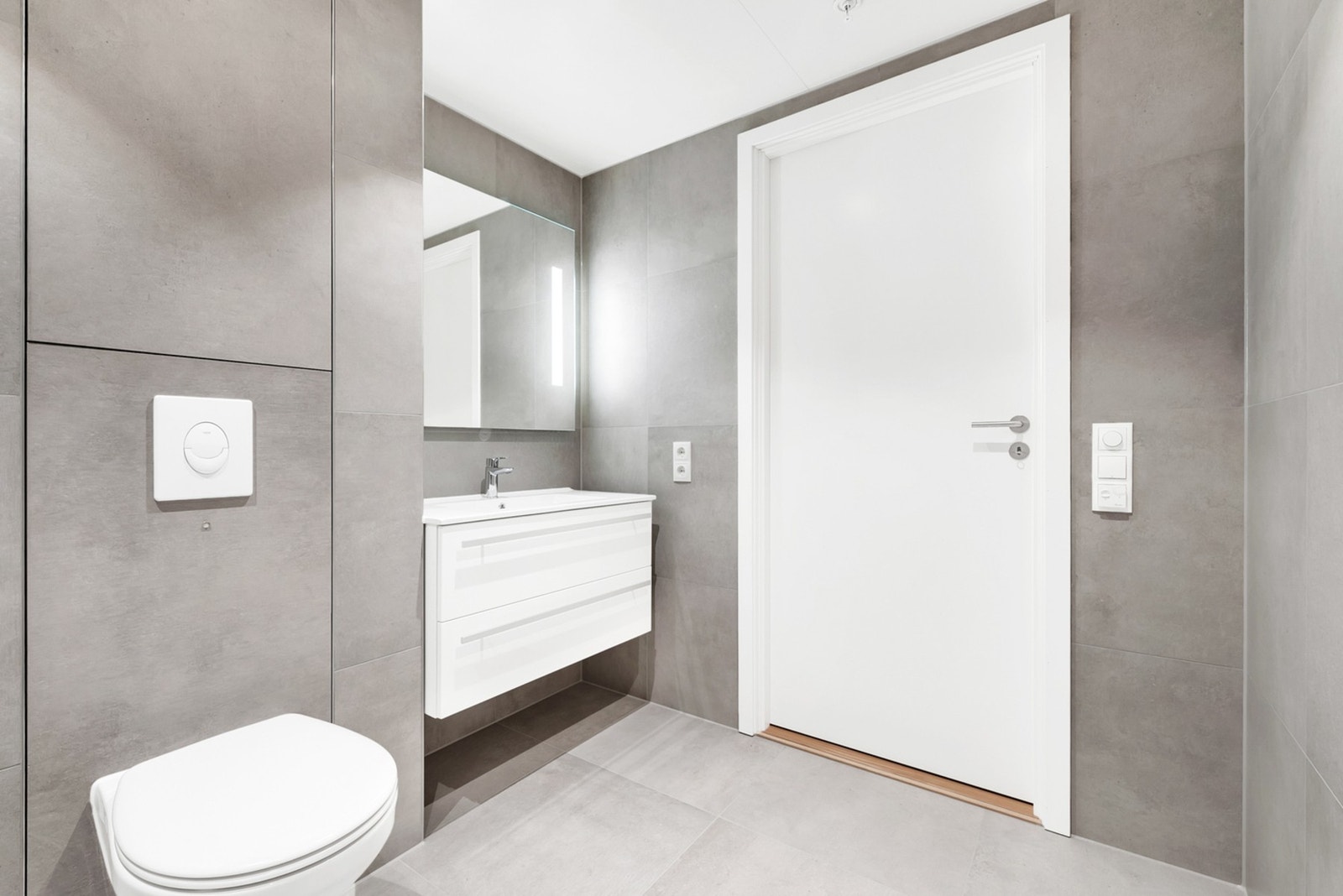 Badet har vegghengt servant med skuffer, ovenpåliggende servant og ett-greps armatur. Speil med sidelys. Dusjhjørne med dører og vegghengt dusjarmatur. Vegghengt toalett. Galleribilde