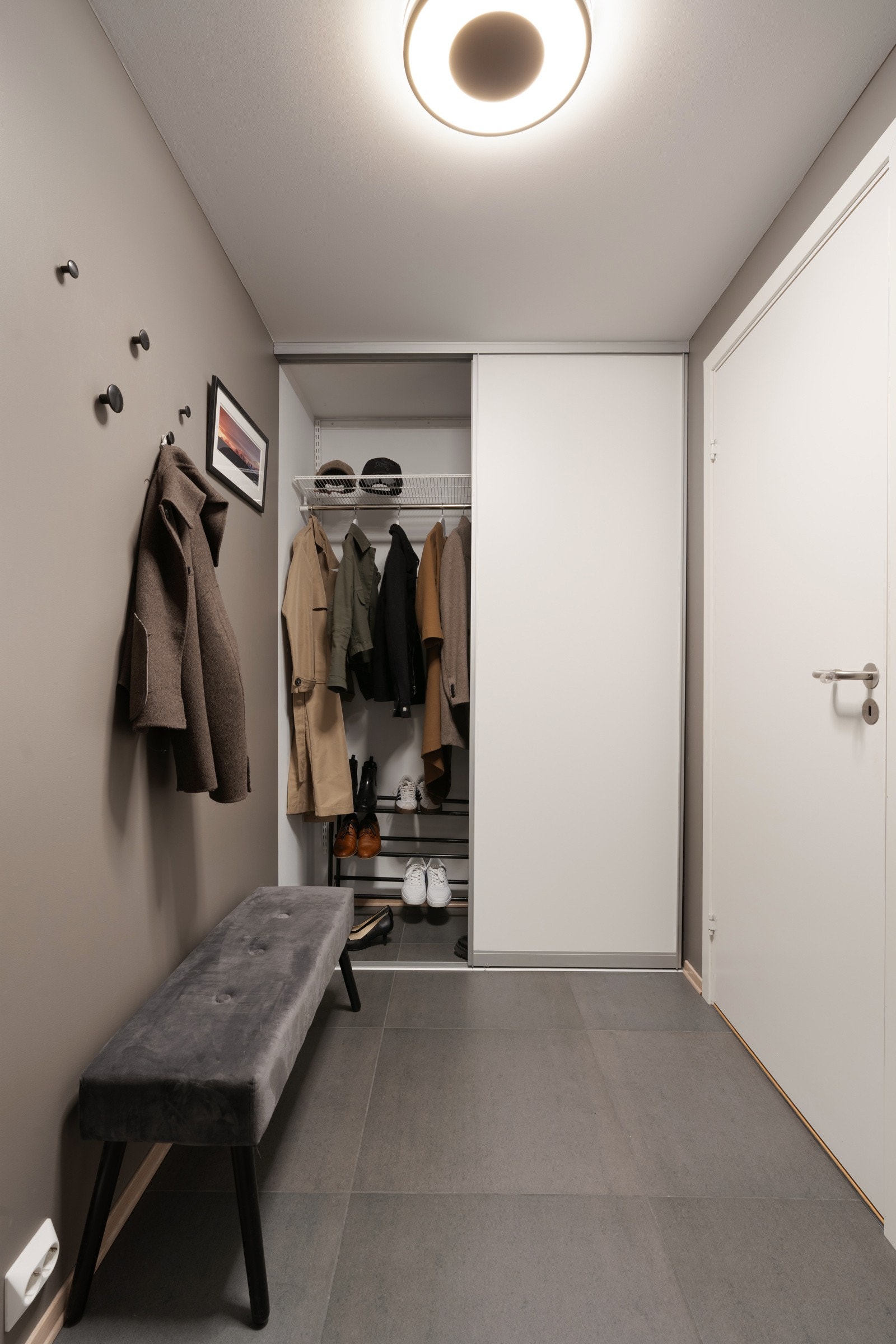 Entreen har store fliser (60x60 cm) med gulvvarme, en lun gråfarge (Band Stone fra Jotun) på veggene og stor skyvedørsgarderobe med god oppbevaringsplass for sko og yttertøy.