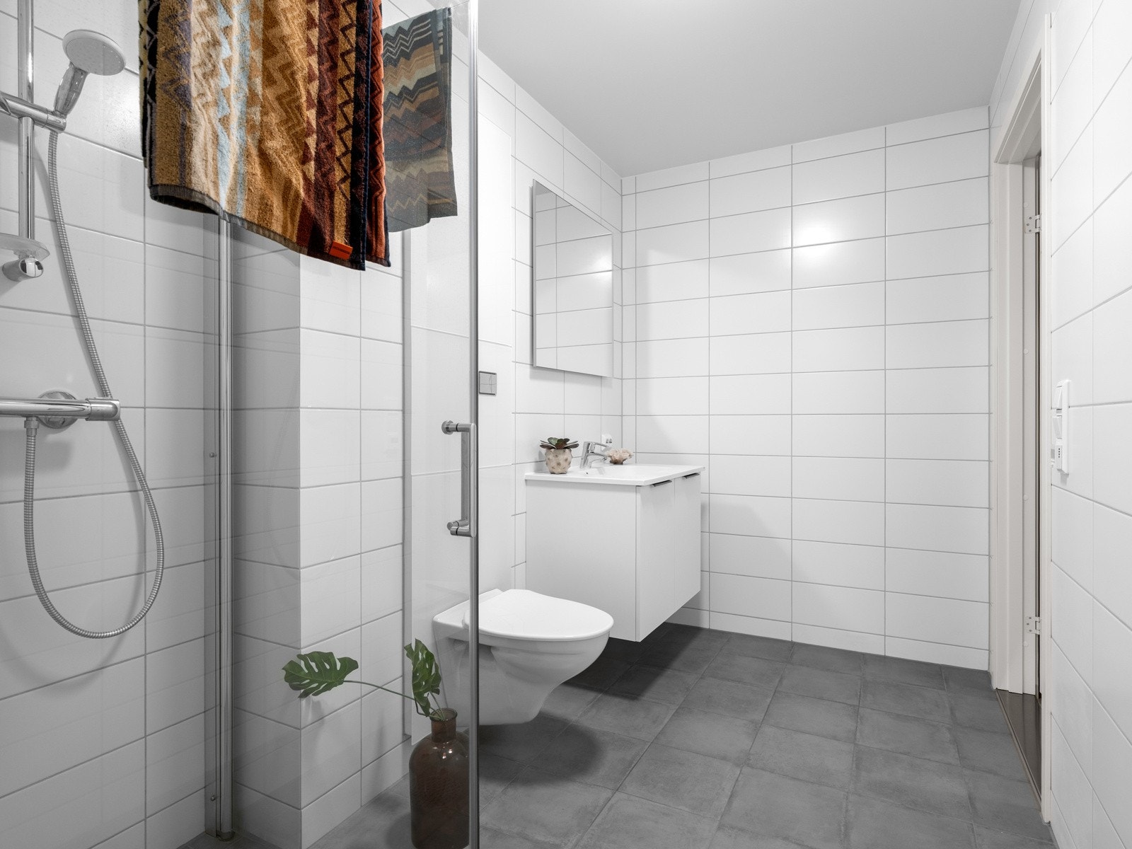 Badet har dusjhjørne med innfellbare glassdører, servant med underskap og speil Galleribilde