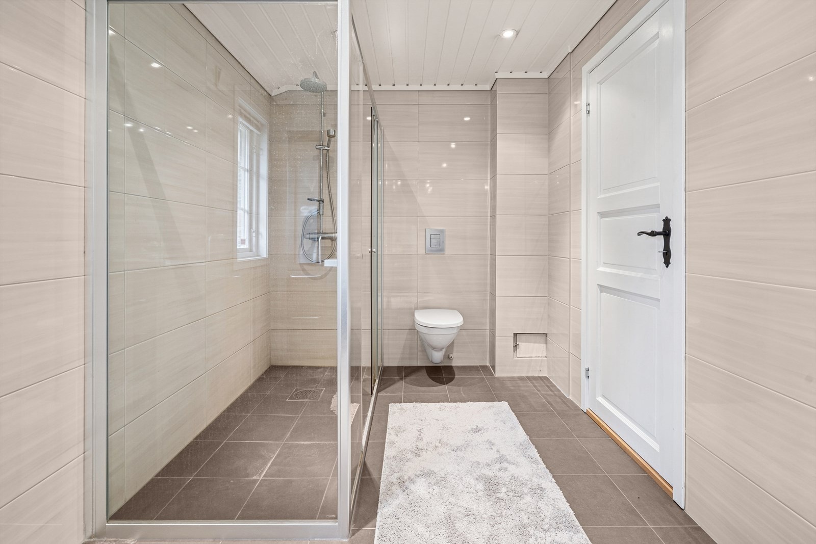 Hytta har et stilrent og innbydende bad med flislagt gulv og vegger Galleribilde